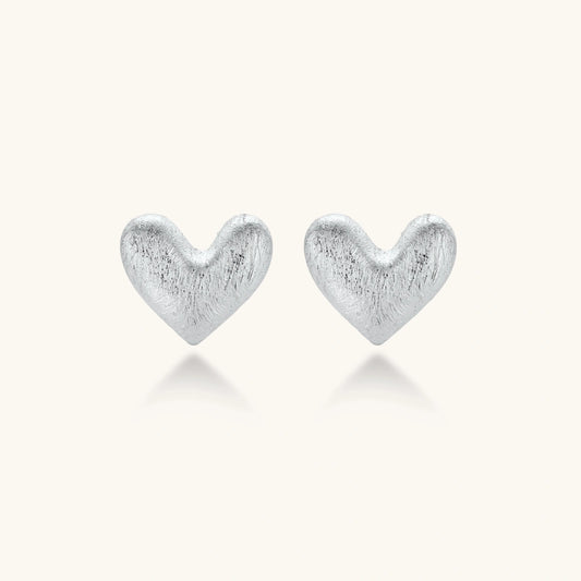 Pair of brushed platinum-plated 925 sterling silver puffy heart stud earrings on a cream background.