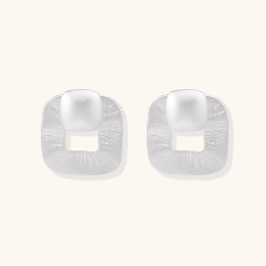 Pair of geometric sterling silver earrings with frosted square frames and glossy rounded studs on white background
