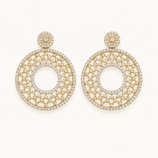 A pair of large gold-tone dangle earrings paved with clear stones, featuring a circular openwork design and a small round stud at the top, shown on a plain off-white background.