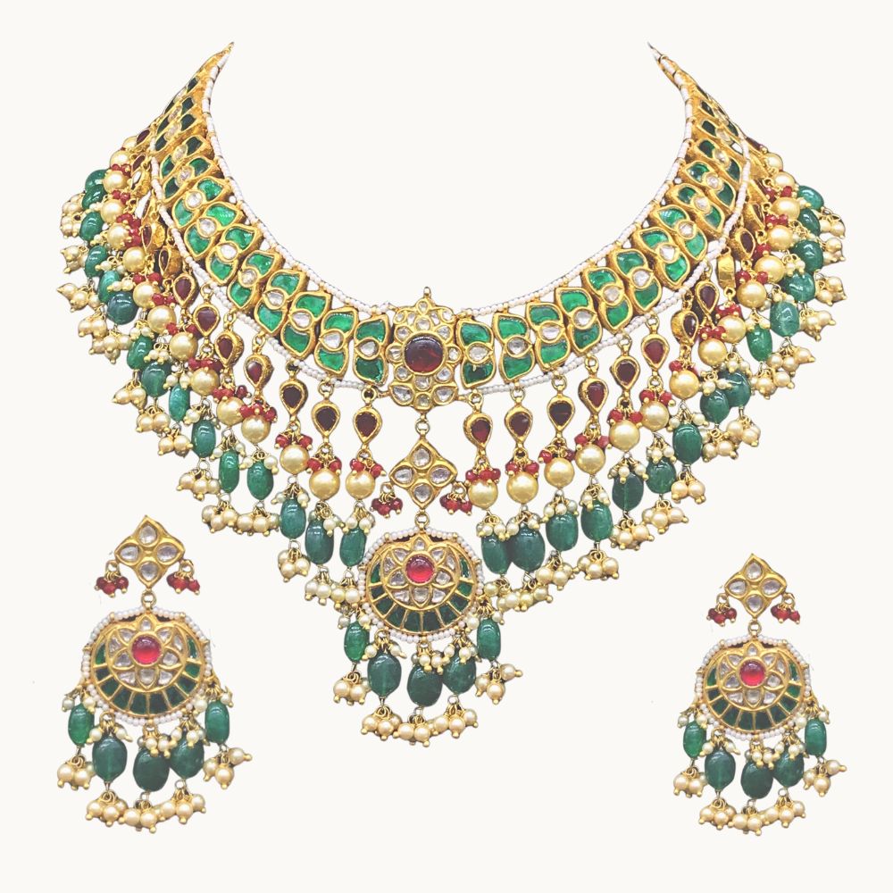 An ornate traditional Indian gold-plated jewelry set featuring a choker necklace and matching drop earrings, embellished with green stones, red stones, and gold-toned bell-shaped charms, shown on a plain light background.