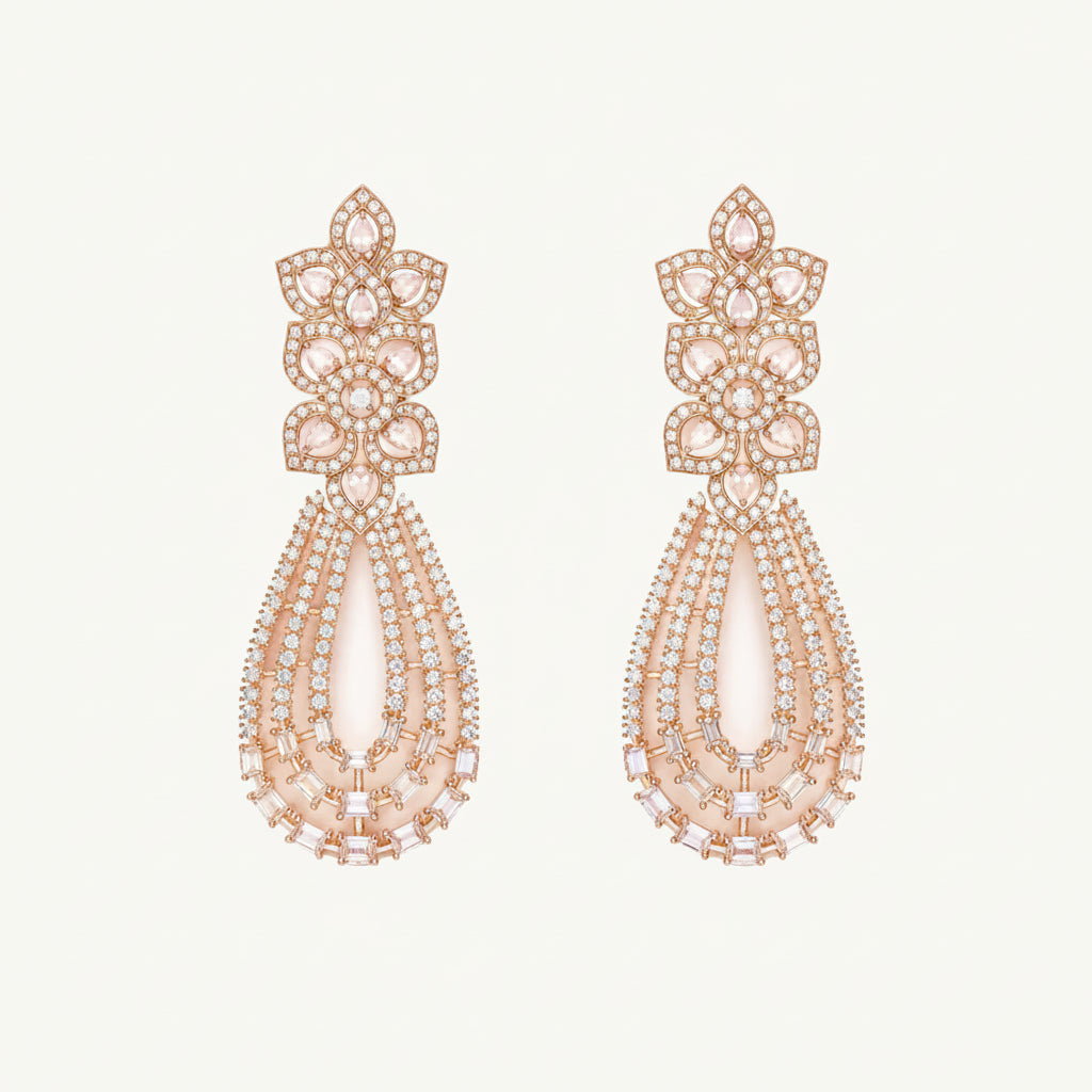 A pair of rose gold statement drop earrings featuring a floral cluster top set with clear stones and a teardrop-shaped lower section with layered clear and pale pink stones, shown on a light cream background.