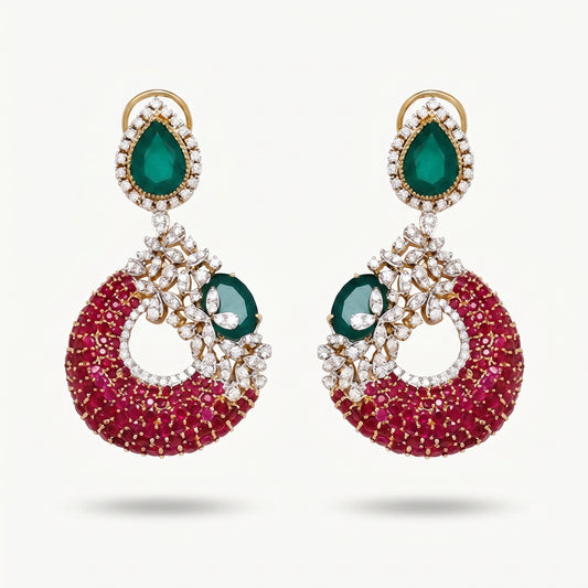 A pair of gold-plated drop earrings featuring a large teardrop-shaped green emerald stone at the top, surrounded by small clear stones, and a crescent-shaped lower section covered in deep pinkish-red stones with a smaller green emerald and clear stone detail.