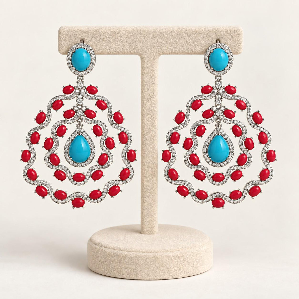 Turquoise and coral chandelier earrings on a cream display stand