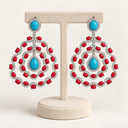 Turquoise and coral chandelier earrings on a cream display stand