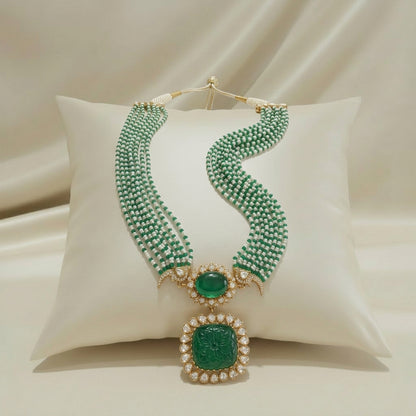 Carved emerald pendant Polki necklace displayed on ivory cushion