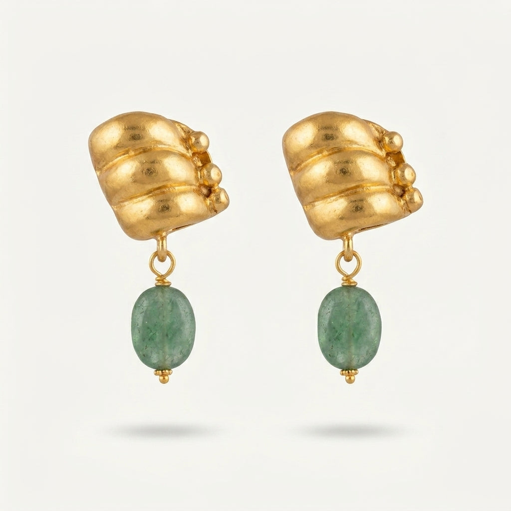 A pair of gold dangle earrings with sculptural, textured gold top pieces and oval green gemstone drops, shown on a light gray background.