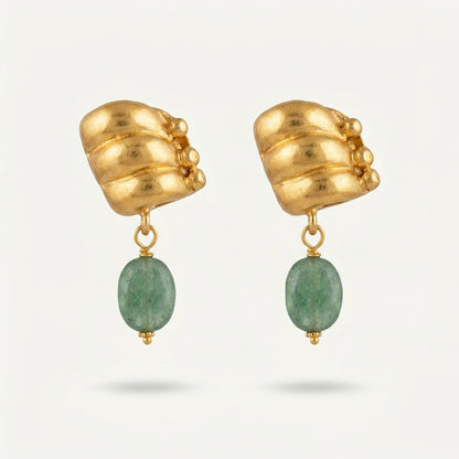 A pair of gold dangle earrings with sculptural, textured gold top pieces and oval green gemstone drops, shown on a light gray background.